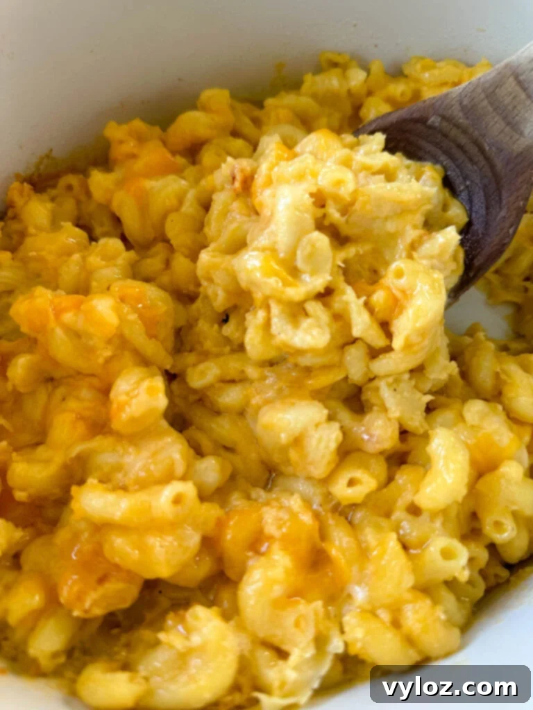Effortless Crockpot Mac and Cheese 8 cheddar cheese mac and cheese in a Crockpot slow cooker with a wooden spoon