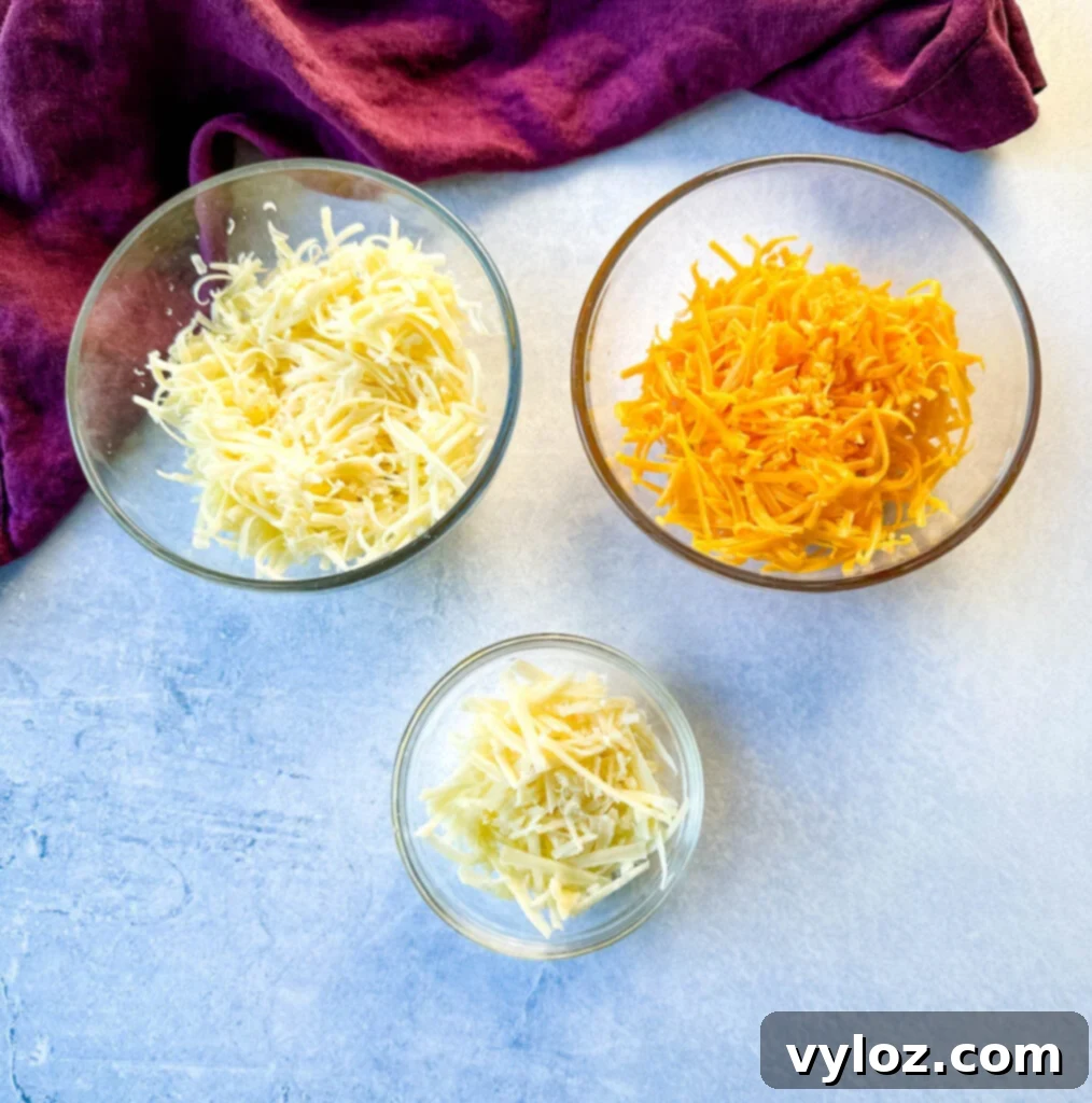 grated cheddar, gruyere, and Parmesan cheese in separate glass bowls