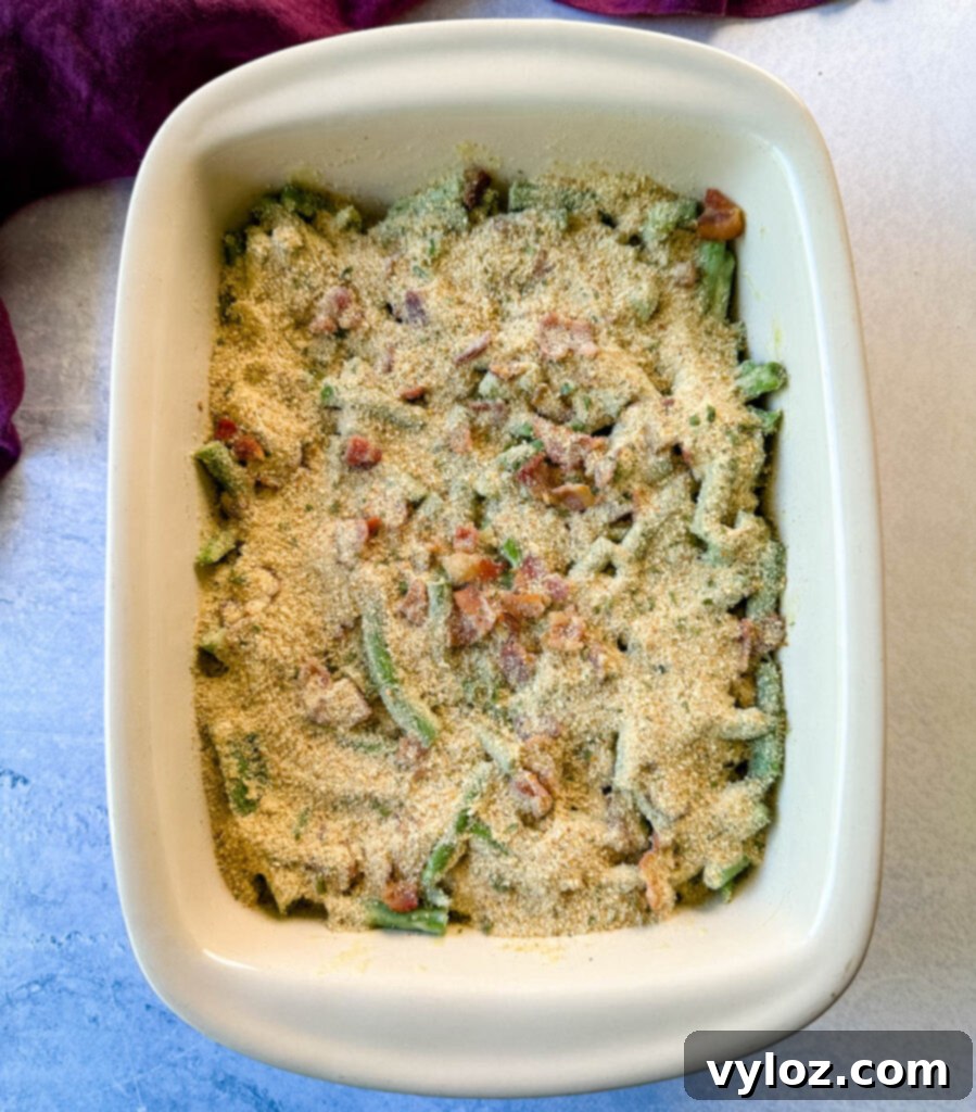 An unbaked green bean casserole with breadcrumbs sprinkled on top in a baking dish