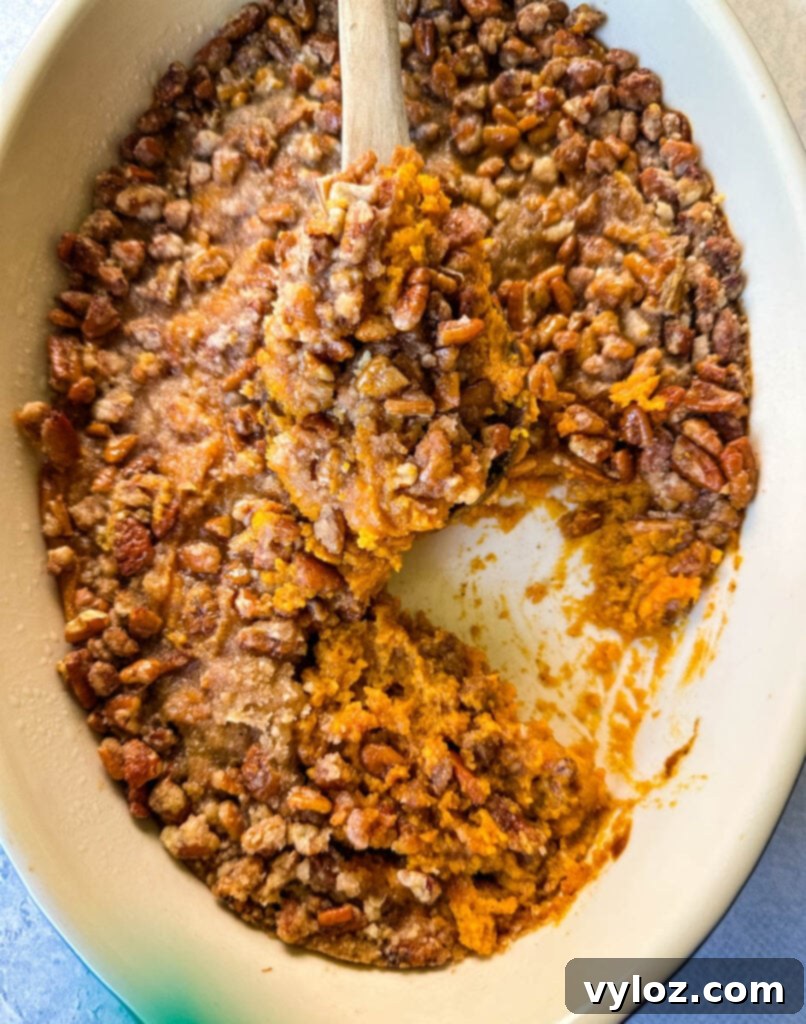 Golden Sweet Potato Pecan Delight 11 Sweet potato casserole with pecan topping in a baking dish with a wooden spoon for serving.