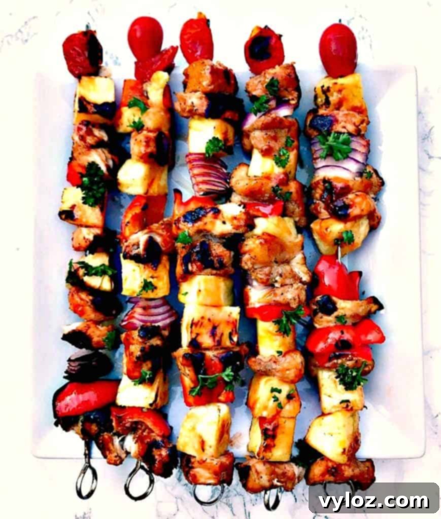 Aloha Grilled Chicken and Pineapple Skewers 5 Individual Hawaiian pineapple chicken kabob skewers served on a white plate, highlighting fresh ingredients.