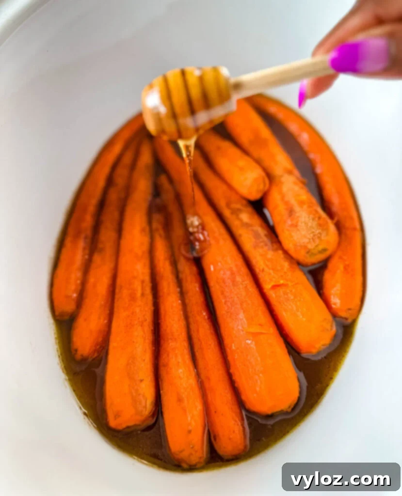 Maple syrup drizzled over glazed carrots in a Crockpot slow cooker, showcasing the rich, golden hue and tender texture.