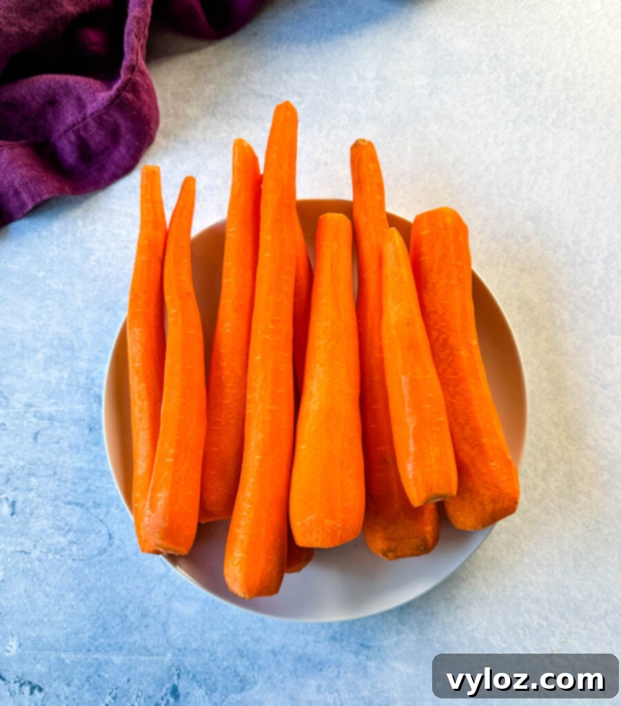 A pile of perfectly peeled carrots on a white plate, highlighting their smooth texture and bright orange color.