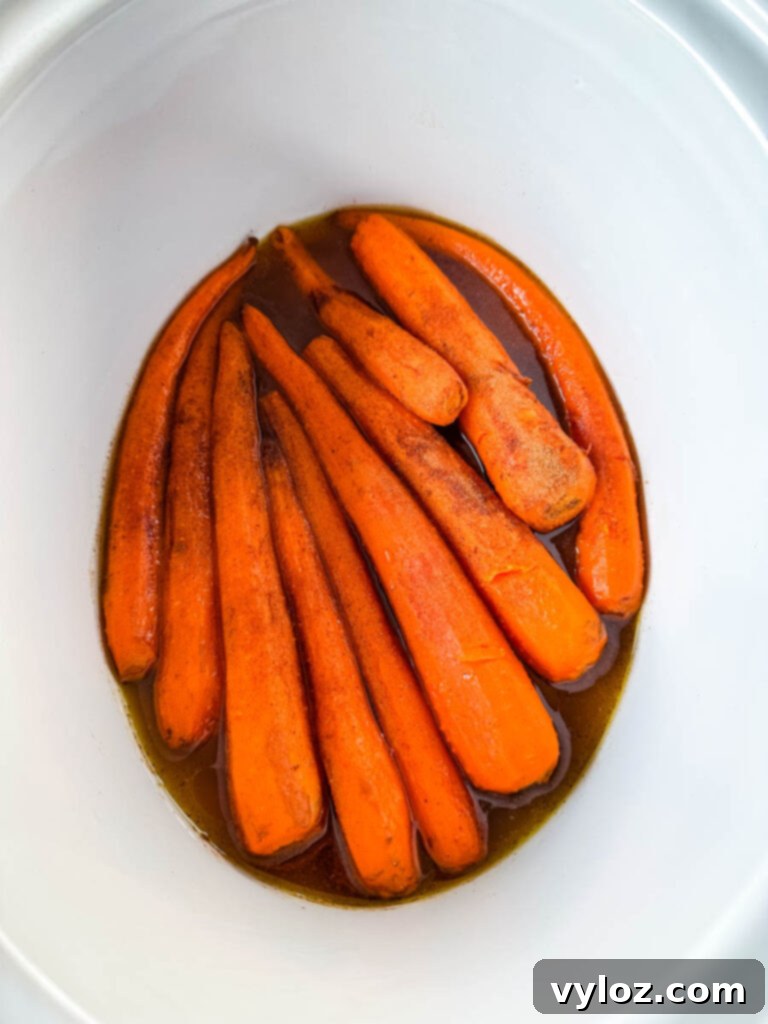 Close-up of maple glazed carrots simmering in a Crockpot slow cooker, glistening with the sweet glaze.