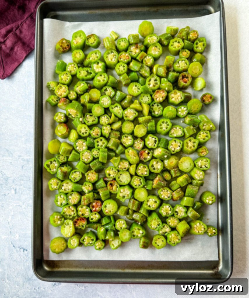 Seasoned fresh okra spread in a single layer on a parchment-lined baking sheet