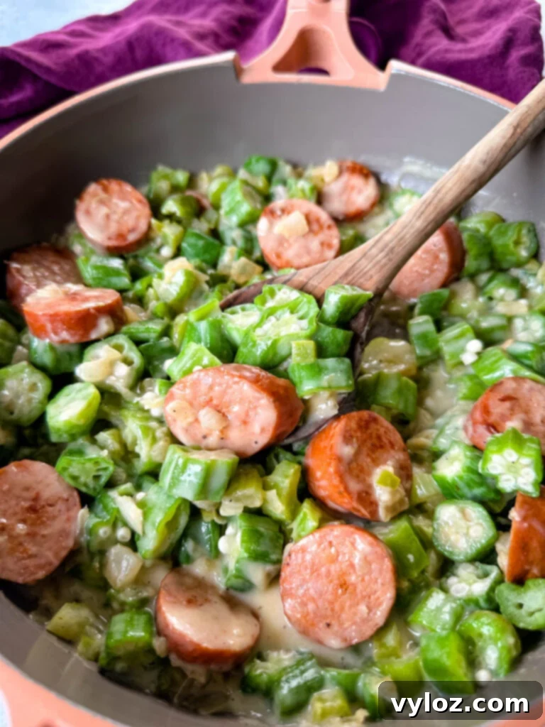 Smothered okra with savory sausage and creamy Creole gravy in a skillet