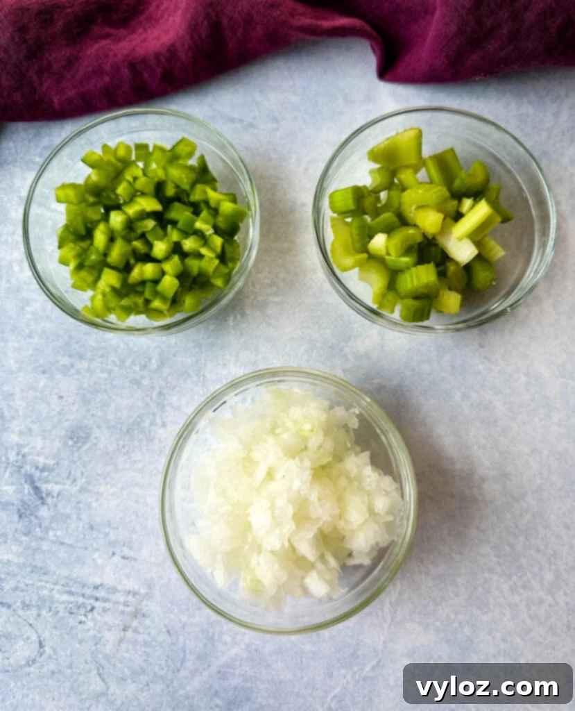 Diced green bell peppers, celery, and onions, known as the Holy Trinity, in separate glass bowls