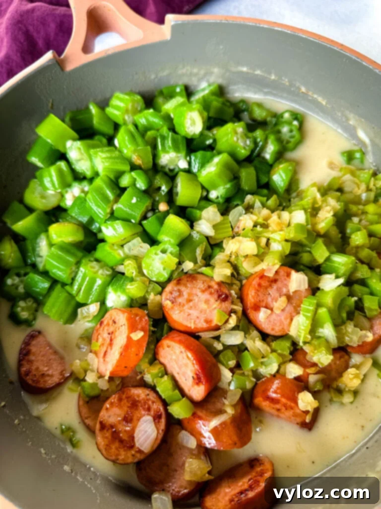 Smothered okra with sausage and gravy in a skillet with a wooden spoon, ready to serve