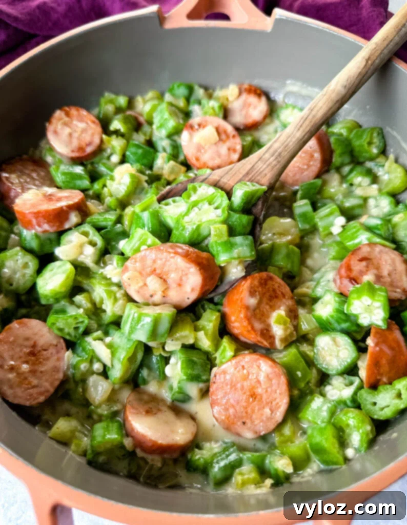 Smothered okra with sausage and gravy in a skillet with a wooden spoon, garnished and ready