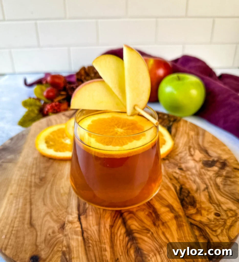 A festive apple cider bourbon cocktail garnished with orange and apple slices in a glass