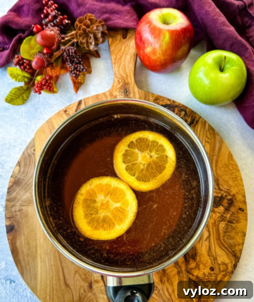 Ingredients for apple cider bourbon cocktail, including oranges and cinnamon, in a saucepan