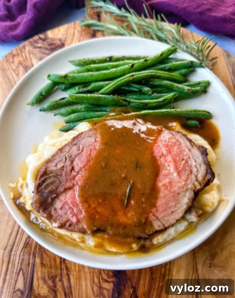 sliced eye of round roast beef on a plate with mashed potatoes, green beans, and au jus gravy