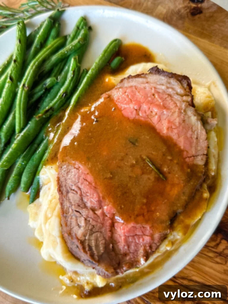sliced eye of round roast beef on a plate with mashed potatoes, green beans, and au jus gravy
