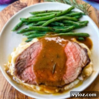 sliced eye of round roast beef on a plate with mashed potatoes, green beans, and au jus gravy