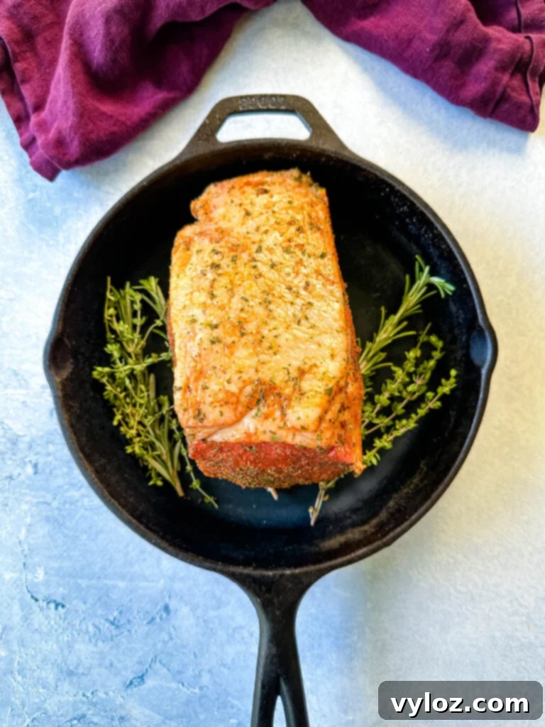 raw eye of round roast beef in a cast iron skillet with fresh herbs