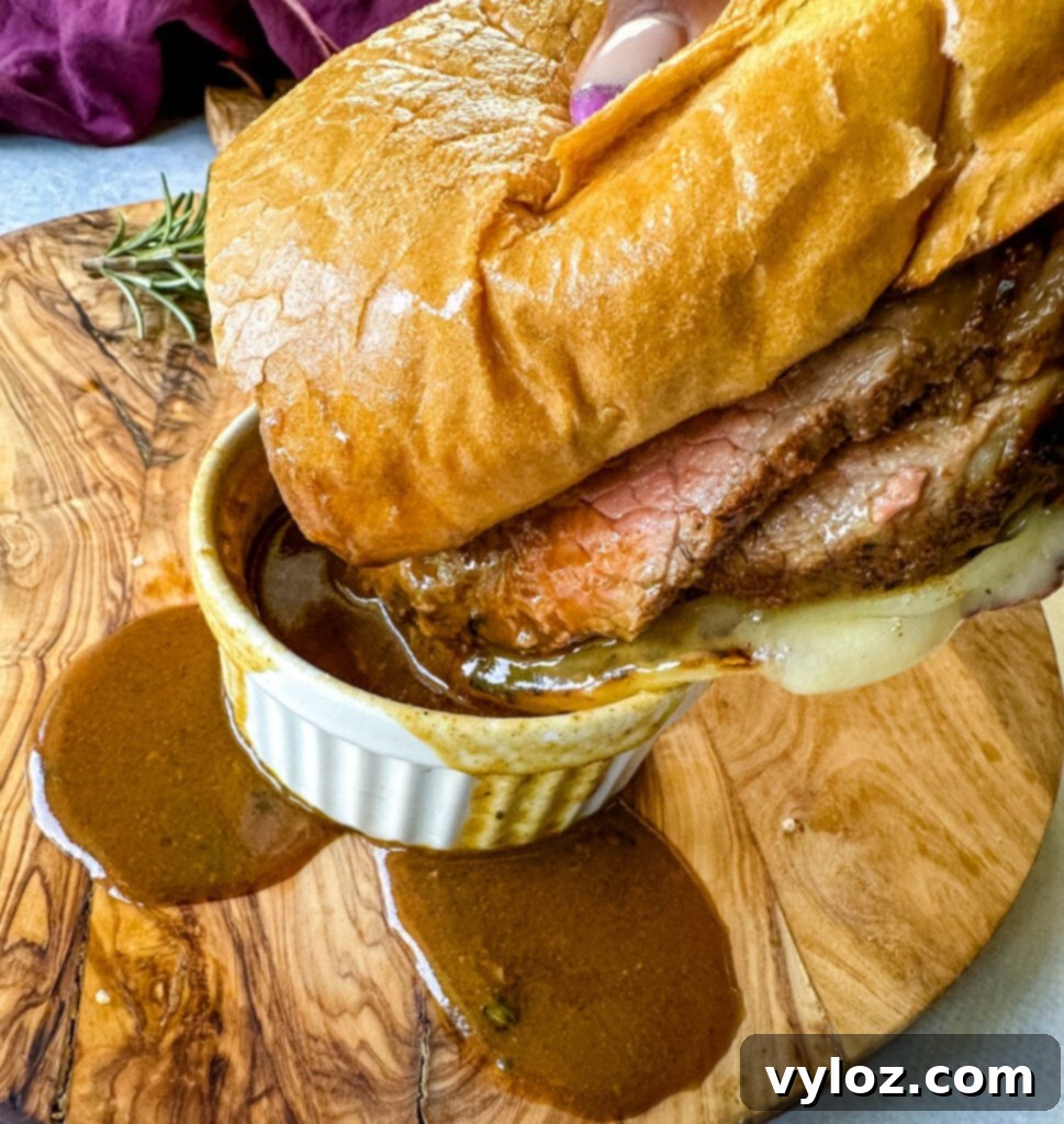 person holding French dip roast beef sandwich dripped in au jus sauce