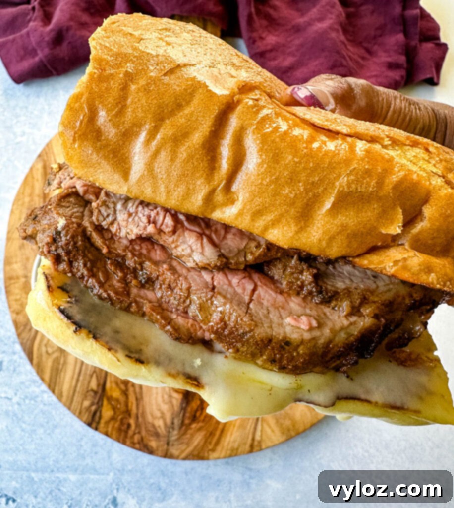person holding roast beef sandwich with swiss cheese