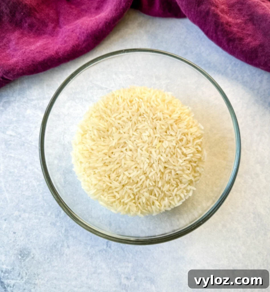 A glass bowl filled with dry, uncooked long-grain white rice, ready to be prepared as a classic accompaniment to Southern Red Beans and Rice.