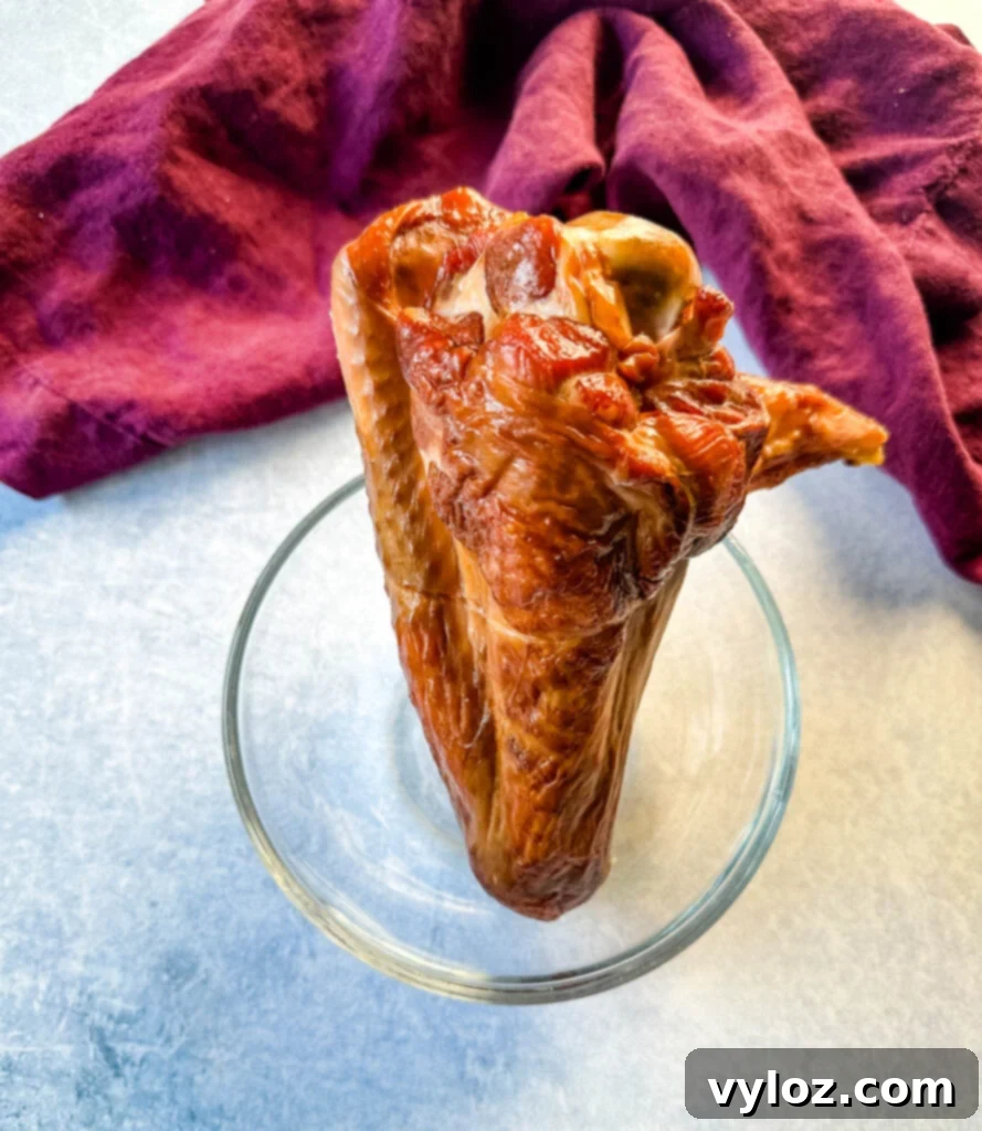 A smoked turkey wing resting in a glass bowl, showcasing its rich, deep brown color, signifying its readiness to impart smoky flavor to a dish.