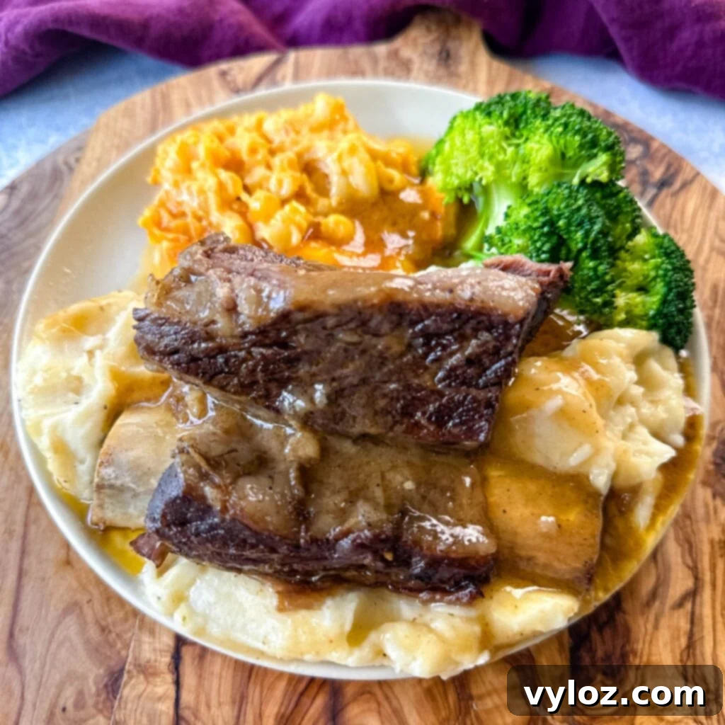 braised beef short ribs drizzled in gravy with mashed potatoes, mac and cheese, and broccoli on a plate
