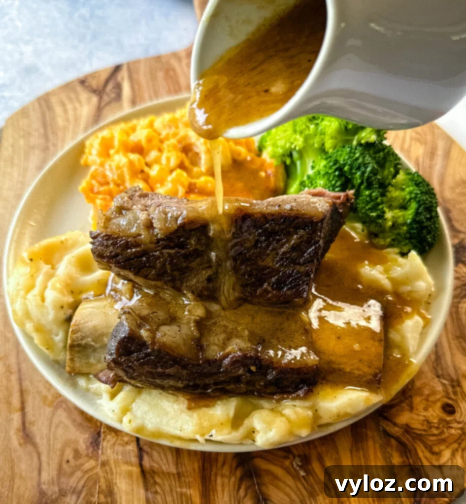 braised beef short ribs drizzled in gravy with mashed potatoes, mac and cheese, and broccoli on a plate
