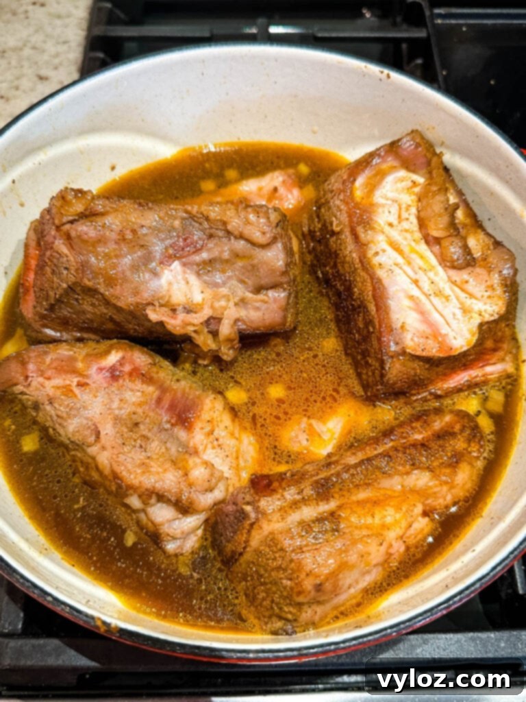 uncooked braised beef short ribs in a Dutch oven with broth