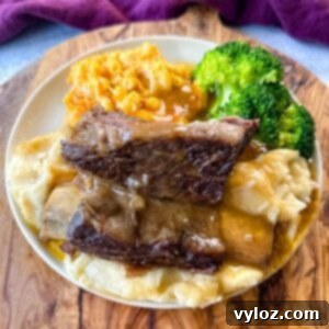 braised beef short ribs drizzled in gravy with mashed potatoes, mac and cheese, and broccoli on a plate