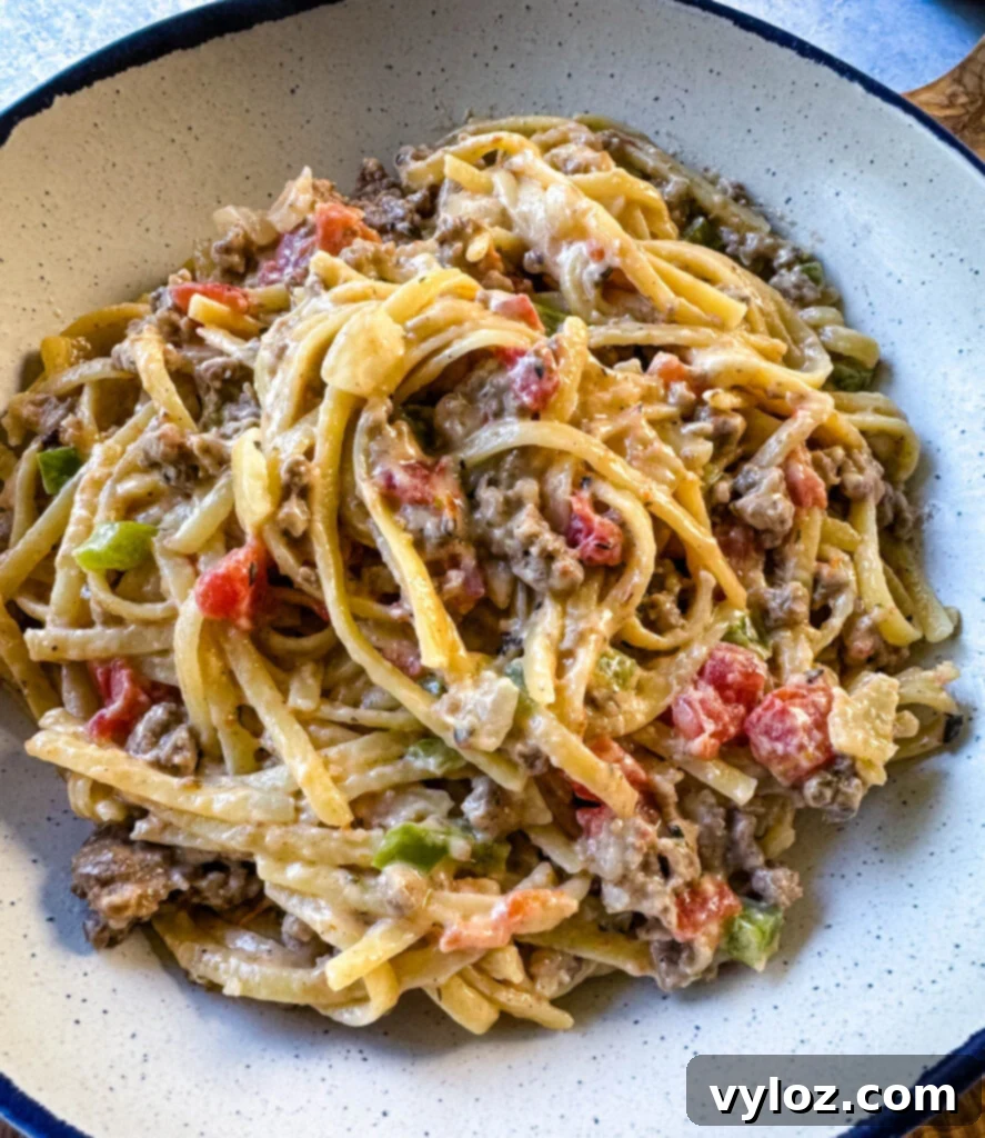 Creamy ground beef alfredo pasta served in a white bowl, garnished with fresh parsley.