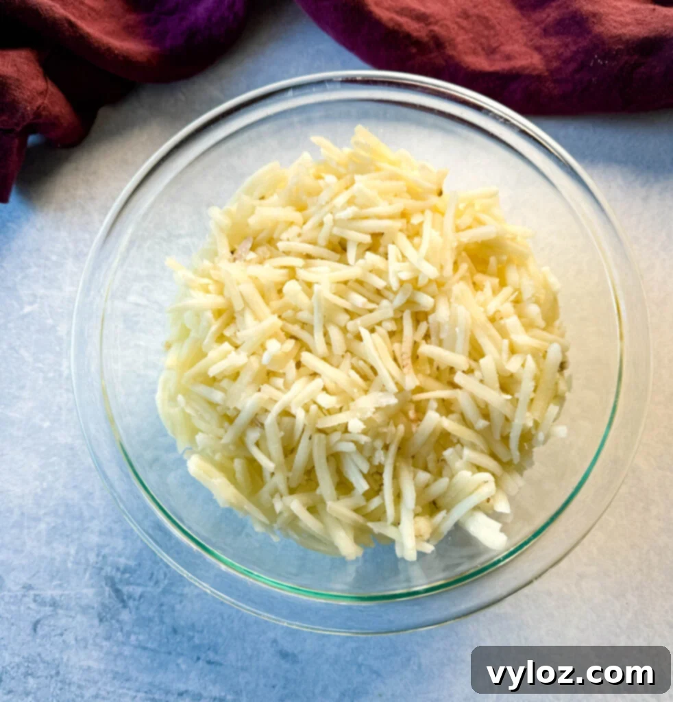 Frozen shredded hash browns in a clear glass bowl, showcasing their texture before thawing.