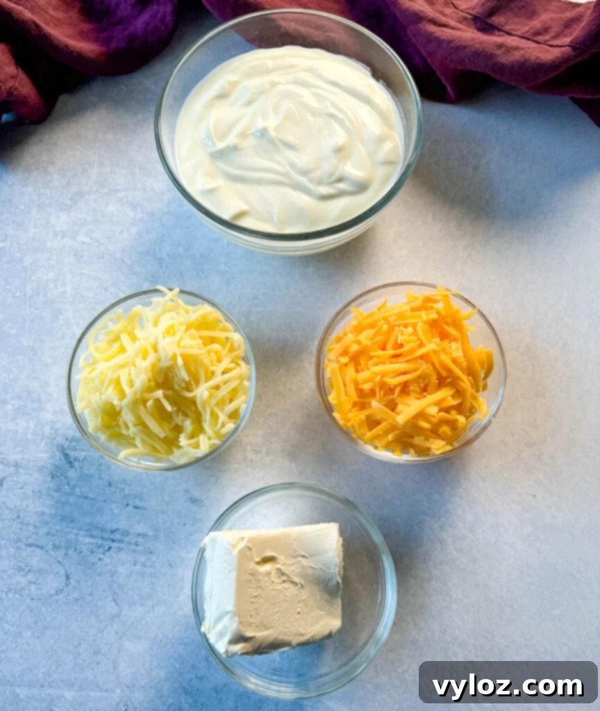 Bowls of sour cream, grated mozzarella, grated cheddar, and cream cheese, showcasing key dairy ingredients for the casserole.