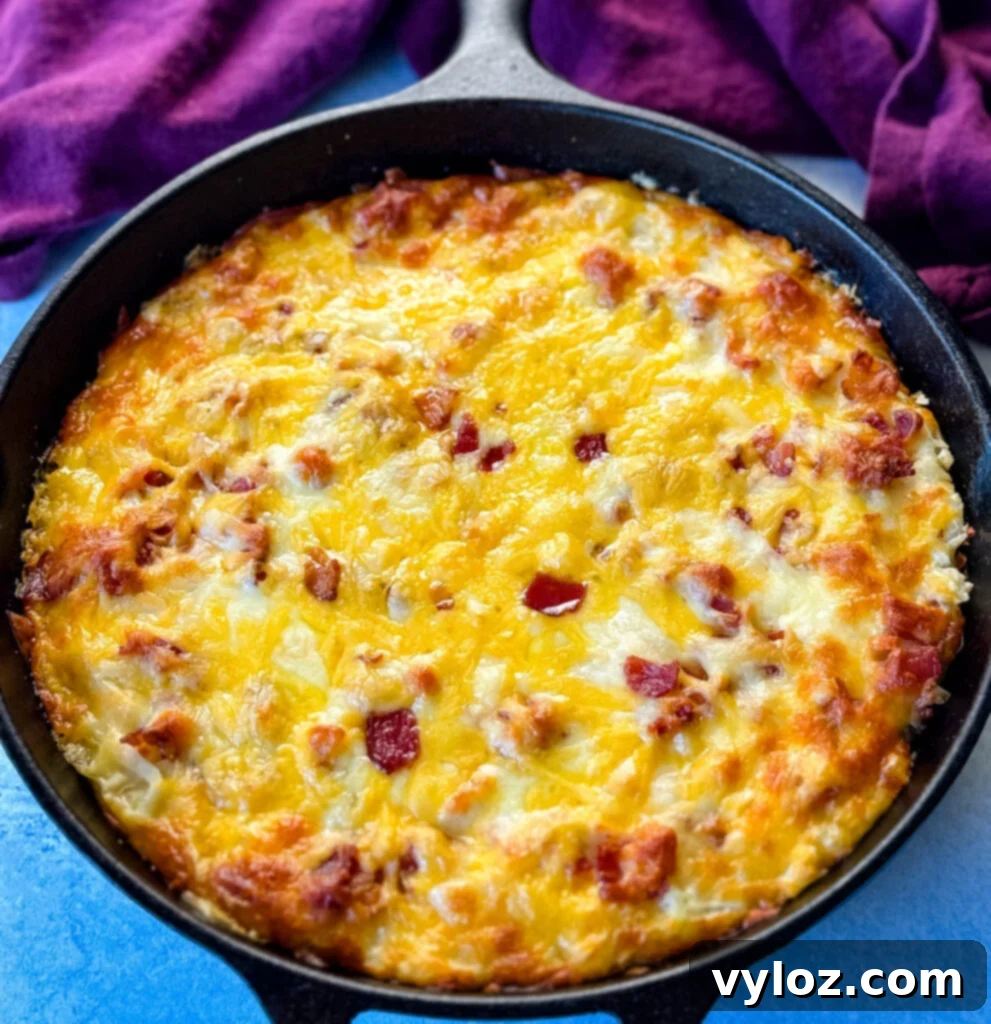 A warm hash brown casserole with bacon and melted cheese, served directly in a cast iron skillet.