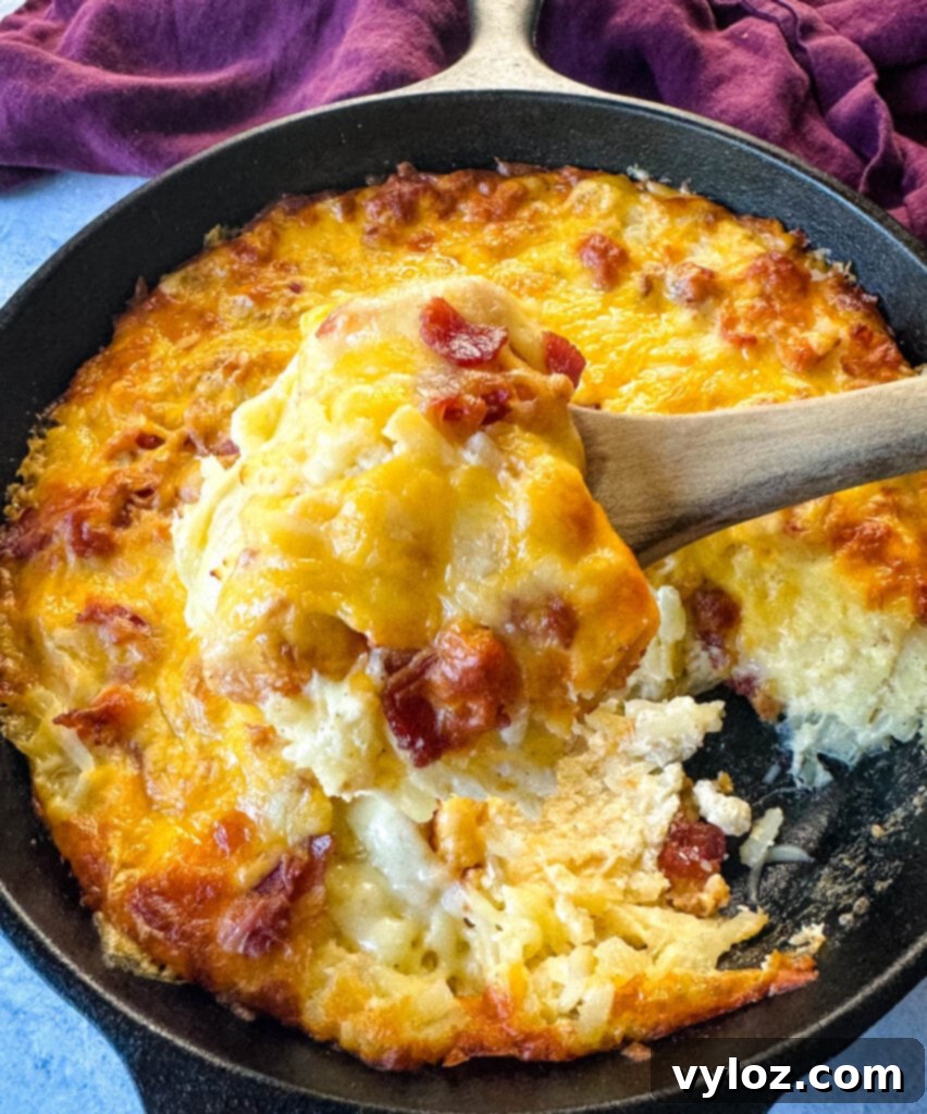 A wooden spoonful of golden hash brown casserole with bacon and melted cheese, freshly baked in a cast iron skillet.