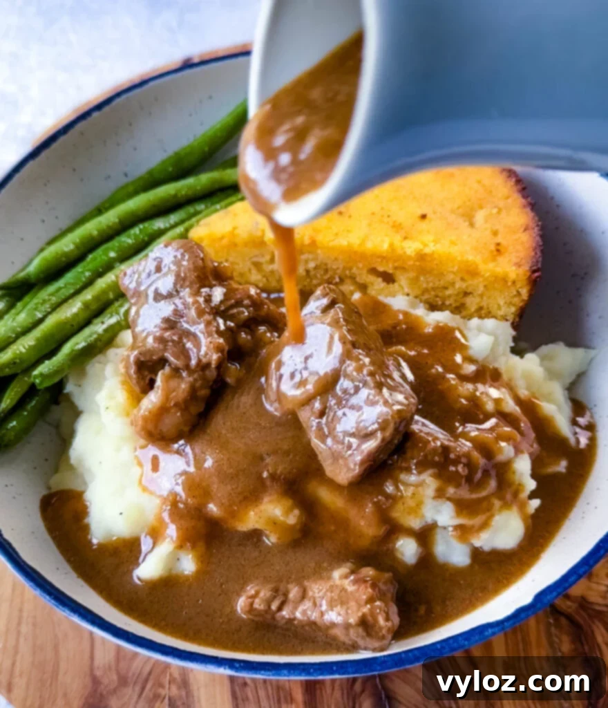 Rich brown gravy generously drizzled over tender beef tips, accompanied by vibrant green beans, a slice of golden cornbread, and creamy mashed potatoes in a cozy serving bowl, highlighting a perfect comfort meal.