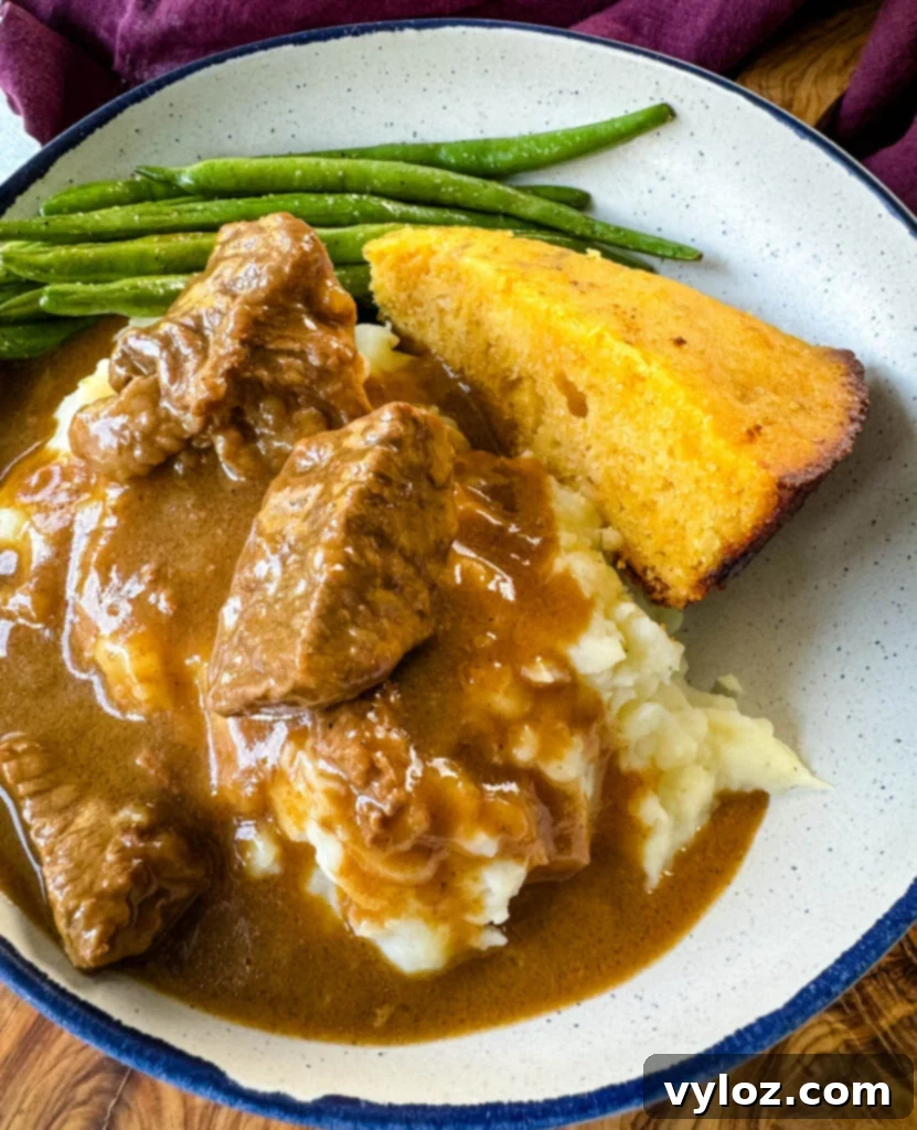 A hearty and appealing serving of beef tips and gravy, paired with fluffy mashed potatoes, vibrant green beans, and a slice of cornbread, presented in a bowl, perfect for a comforting family meal.