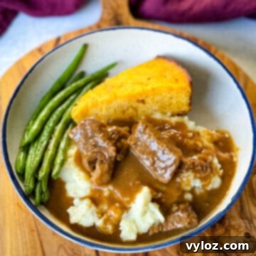 Hearty beef tips and rich brown gravy served with green beans and a slice of cornbread in a rustic bowl, presenting a classic comfort food meal.