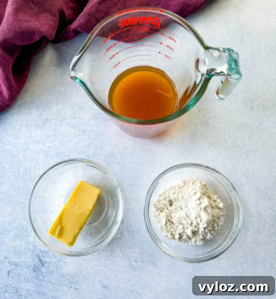 Three glass bowls displaying essential ingredients for the gravy: savory beef broth, rich unsalted butter, and versatile all-purpose flour, neatly arranged for the cooking process.