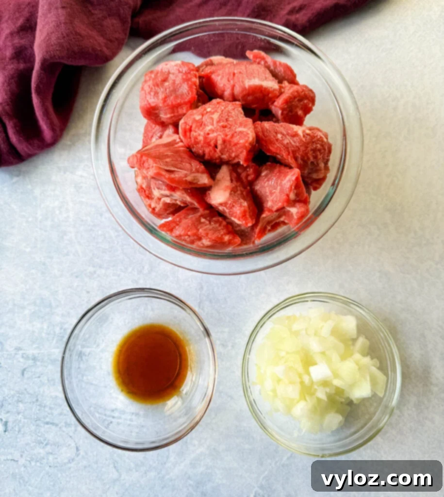 A trio of glass bowls showcasing essential ingredients for beef tips: raw, bite-sized stew meat, finely diced white onions ready for sautéing, and a bottle of rich Worcestershire sauce, illustrating the preparation stage.