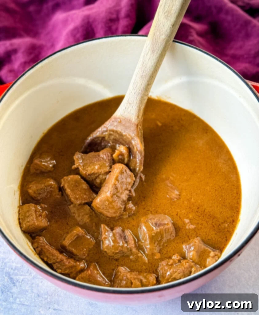 Tender beef tips smothered in rich, homemade brown gravy, simmering gently in a vibrant red Dutch oven, ready to be served as a comforting meal.