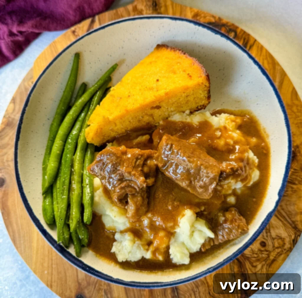 A comforting serving of beef tips and gravy, accompanied by fluffy mashed potatoes, vibrant green beans, and a slice of golden cornbread, neatly arranged in a bowl, showcasing a hearty family meal.