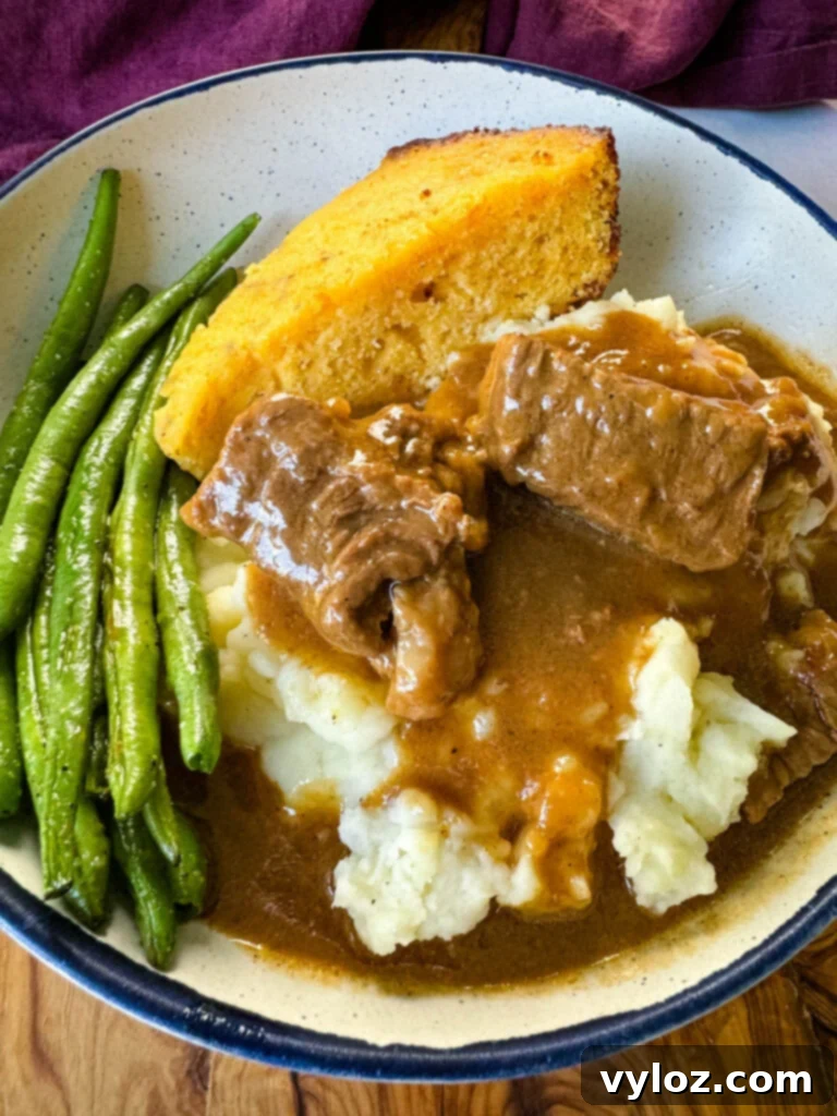 A close-up shot of a cozy bowl filled with tender beef tips and gravy, accompanied by creamy mashed potatoes, crisp green beans, and a golden slice of cornbread, showcasing a comforting and complete meal.