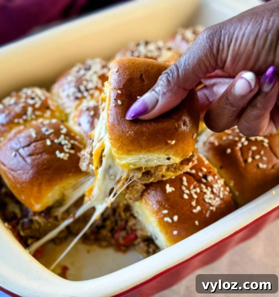 A hand reaching for a perfectly golden King's Hawaiian Slider with melted cheese, showcasing its irresistible appeal