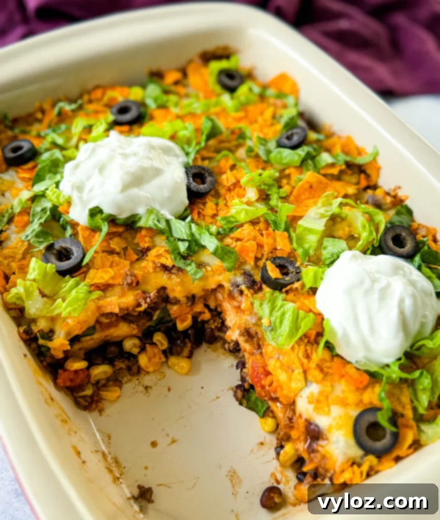 Delicious Taco Bake Casserole in a baking dish, garnished with crushed Doritos, black olives, fresh lettuce, and a dollop of sour cream