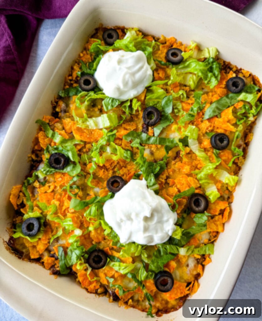 Taco Bake Casserole in a baking dish, beautifully garnished with crushed Doritos, black olives, shredded lettuce, and a generous dollop of sour cream.