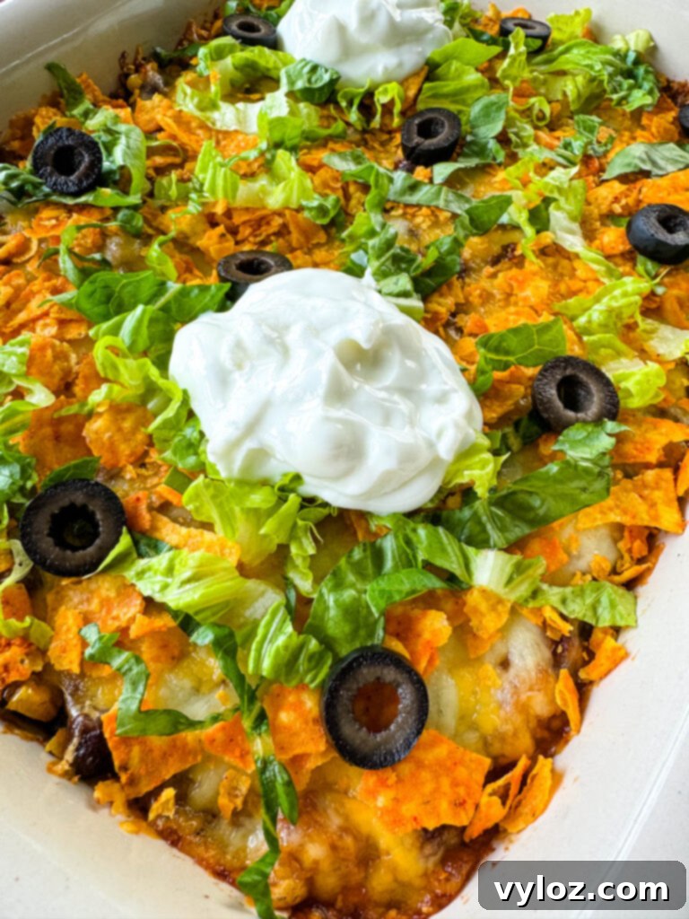A side view of the baked Taco Bake Casserole in a ceramic baking dish, topped with Doritos, olives, lettuce, and sour cream, ready to be served.