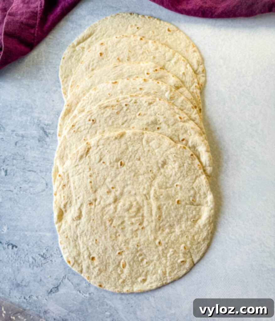 Plain flour tortillas spread out on a flat surface, ready to be torn for the casserole layers.
