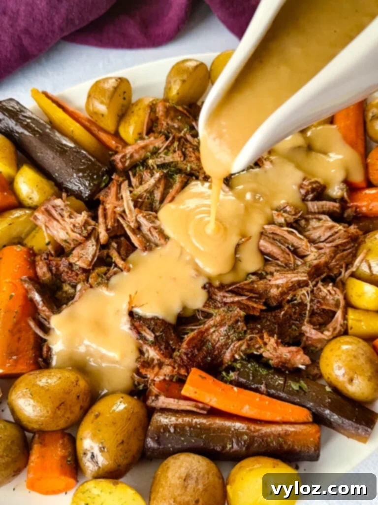 Melt-in-Your-Mouth Slow Cooker Beef Roast 2 cooked beef pot roast, carrots, and potatoes drizzled with gravy on a white plate