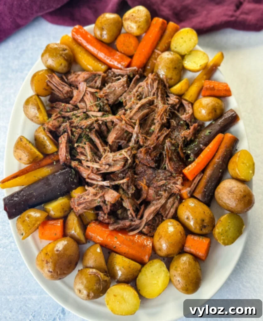 Melt-in-Your-Mouth Slow Cooker Beef Roast 11 cooked beef pot roast, carrots, and potatoes on a white plate
