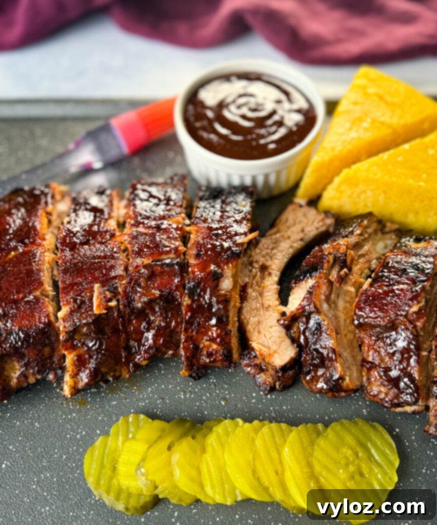 Fall-Off-The-Bone Oven Baby Back Ribs 2 oven baked ribs on a sheet pan with cornbread, BBQ sauce, and pickles