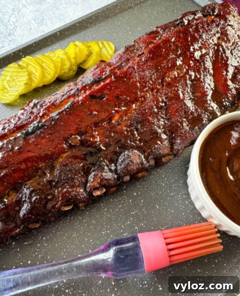Fall-Off-The-Bone Oven Baby Back Ribs 11 cooked ribs with BBQ sauce on a plate with pickles