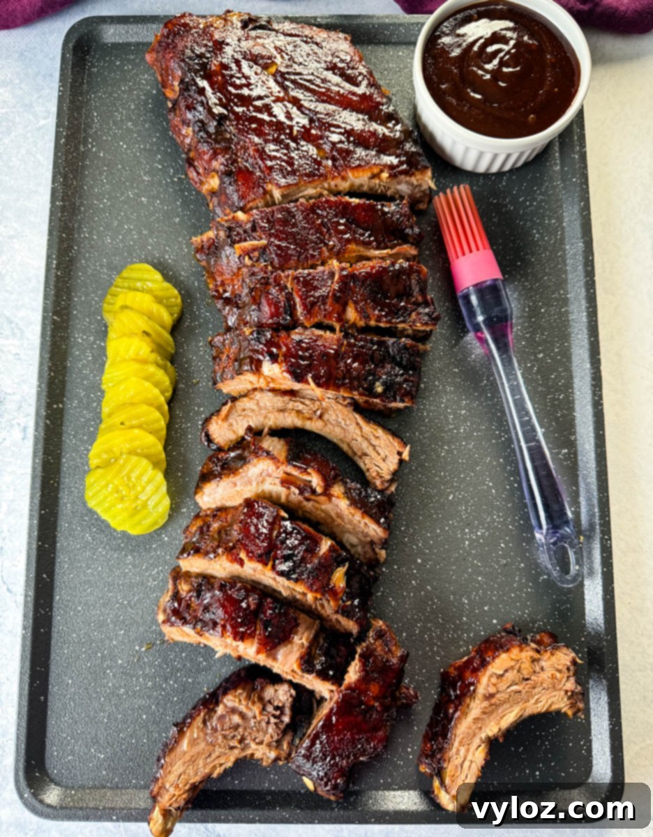 Fall-Off-The-Bone Oven Baby Back Ribs 12 oven baked ribs on a sheet pan with BBQ sauce and pickles